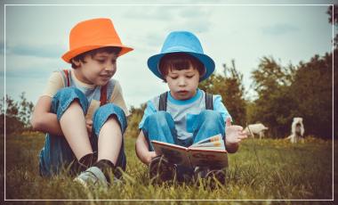 Deux enfants assis dans l'herbe regardent un livre